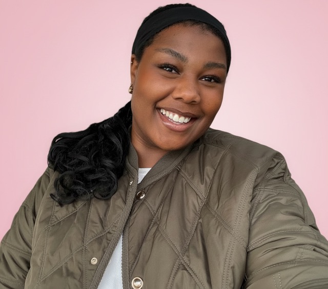 result 3 - Sex in Berlin Smiling woman with a black headband and olive quilted jacket against a pink background.